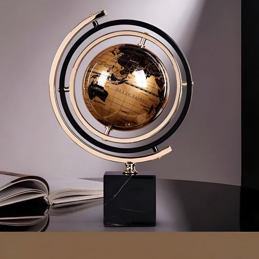 Decorative globe with a black base on a reflective surface, with an open book in the background.