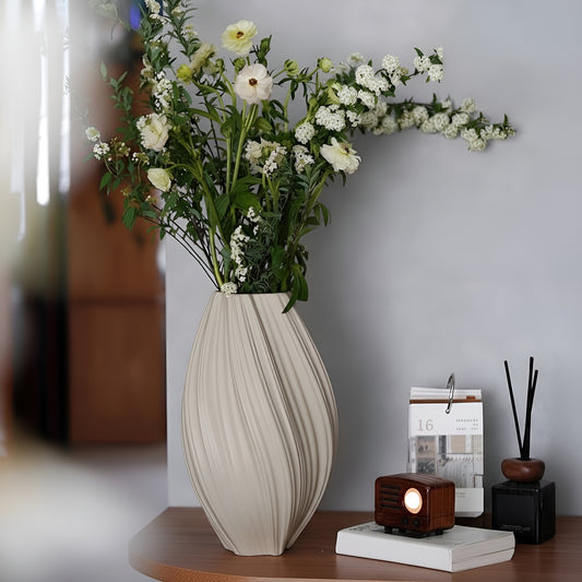 Beige vase with flowers on a wooden surface against a gray wall